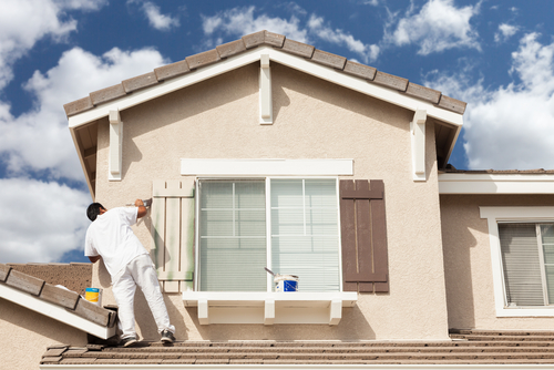 Professional house painting contractor painting shutter on the second floor of a house